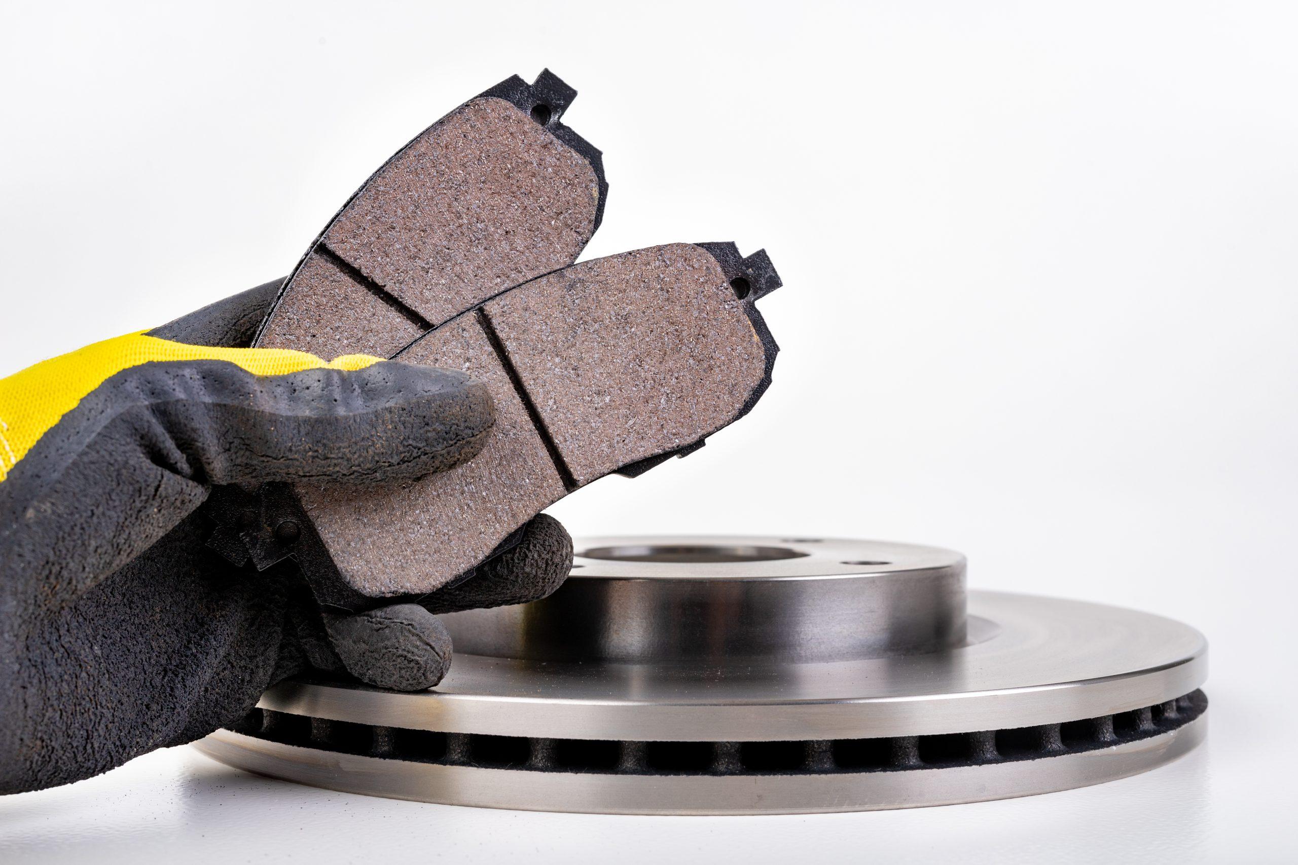Image of a hand with yellow mechanic gloves on, holding brake pads over a rotor.
