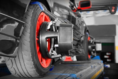 image shows a mechanic putting alignment sensors on a black car on the alignment rack. He is preparing to perform an alignment service on the vehicle.