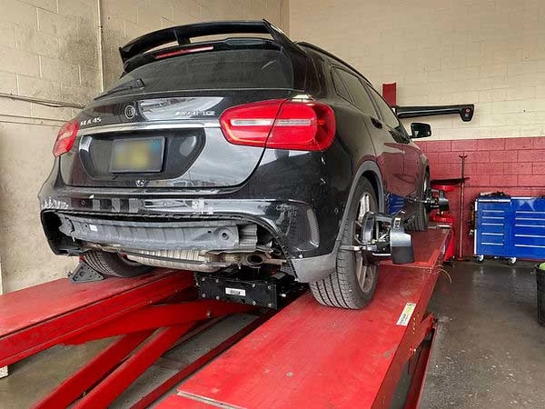 Black Mercedes SUV on alignment rack, mechanic preparing for alignment service