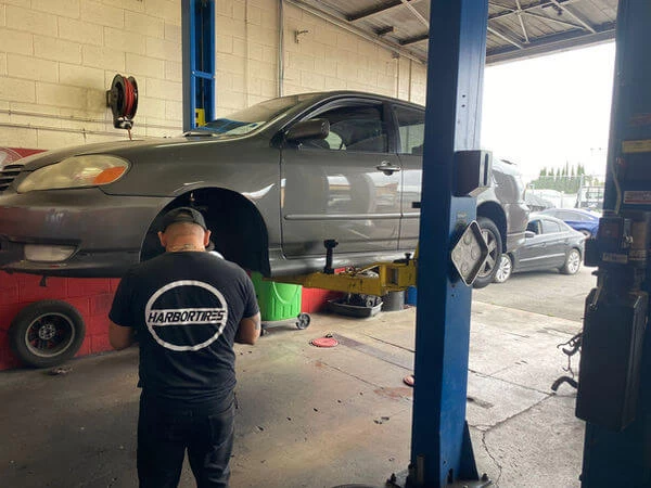 Grey Toyota on 2-post lift, raised with mechanic preparing to service front brakes