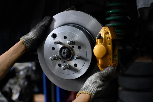 Image shows mechanic hands putting on a caliper back on the car. Finishing his brake job. There is one new slotted rotors and new brake pads.