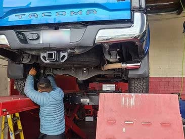 Blue Tacoma on rack, mechanic diagnosing rear driver's side