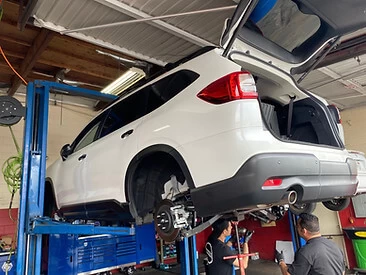 White SUV on a 2-post lift with a customer inspecting its suspension from below