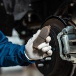 Mechanic holding pads next to the vehicle performing a brake service.
