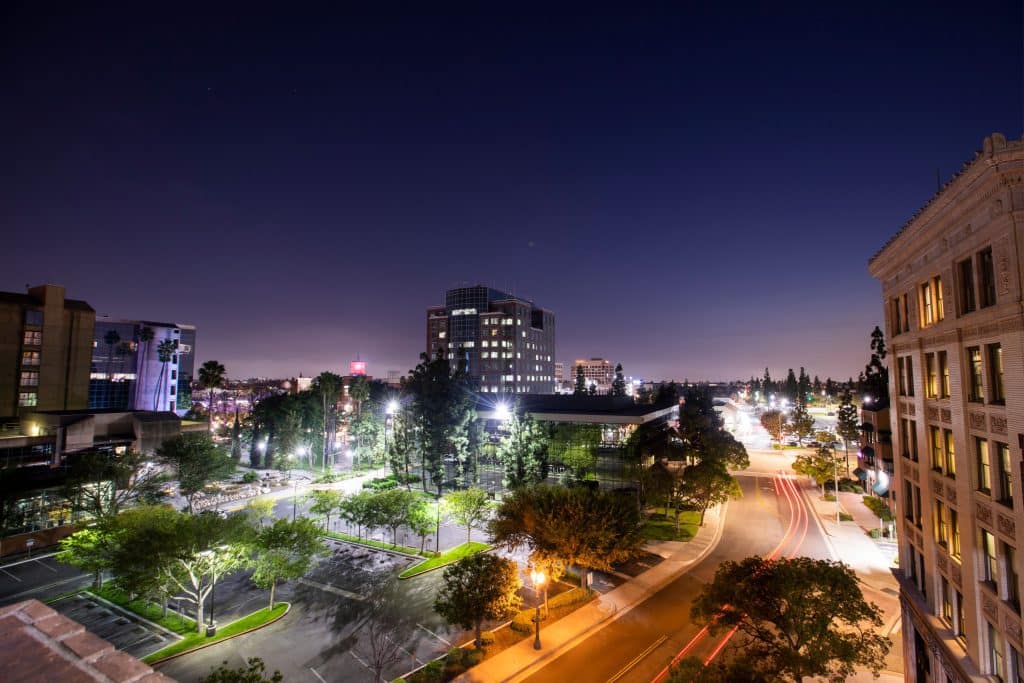 Downtown Anaheim at night with city lights, tree-lined streets, and modern buildings, showcasing the urban atmosphere of Orange County, CA