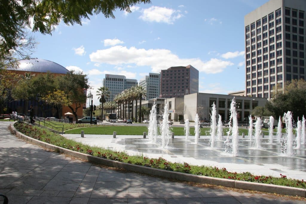 Fountain and cityscape in Fountain Valley, CA with modern buildings, palm trees, and a sunny park setting in Southern California