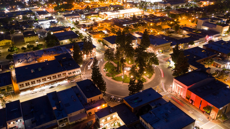 Nighttime aerial view of Old Towne Orange Circle in Orange, CA with city lights illuminating historic buildings and tree-lined roundabout