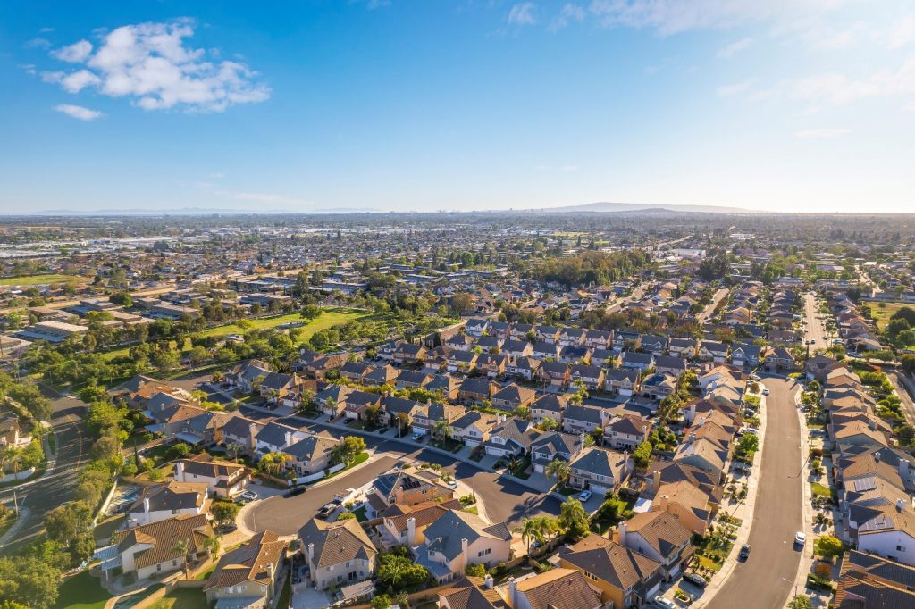 Aerial view of suburban neighborhoods in Cypress, California, featuring rows of homes, tree-lined streets, and a clear, sunny sky.