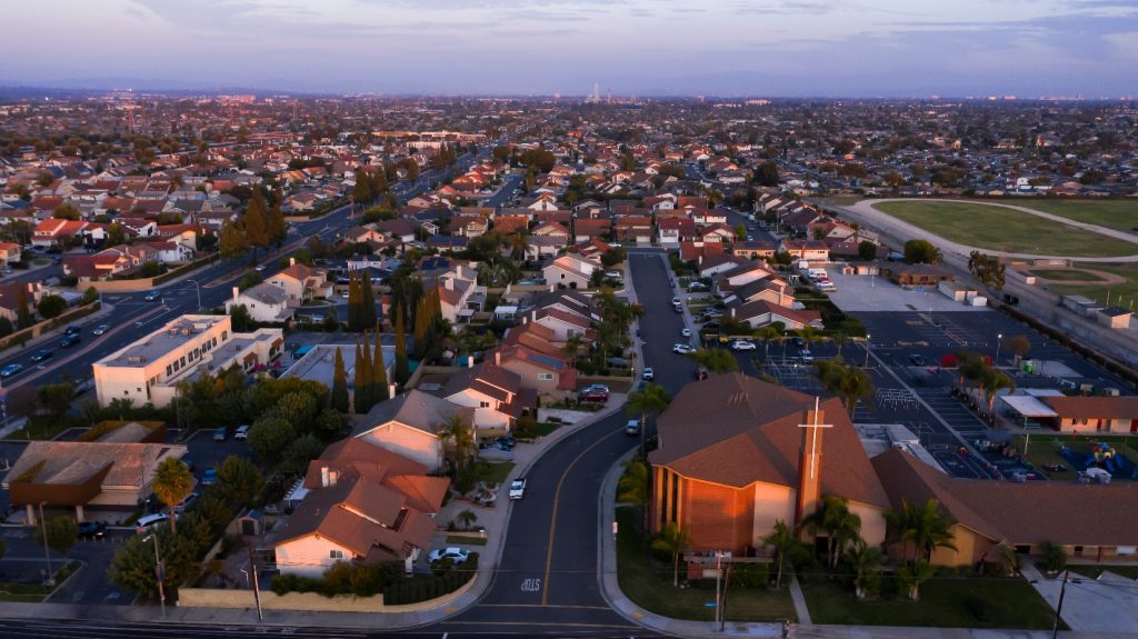 Aerial view of suburban homes and a church in La Palma, California, during sunset with wide cityscape views in the background.