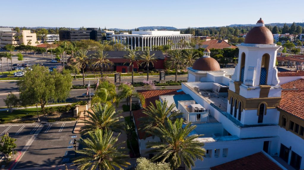 Cityscape of Laguna Woods, California, featuring Spanish-style architecture, palm-lined streets, and modern civic buildings under a clear blue sky.