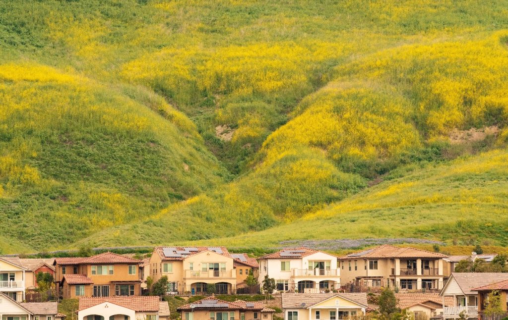 Residential homes at the base of rolling green and yellow wildflower-covered hills in Rancho Mission Viejo, California, during springtime.