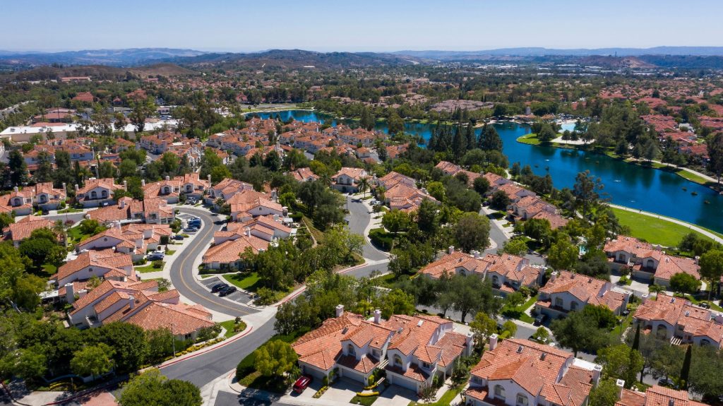 Aerial view of residential neighborhoods and lakes in Rancho Santa Margarita, California, with red-tiled rooftops, green parks, and a clear blue sky.