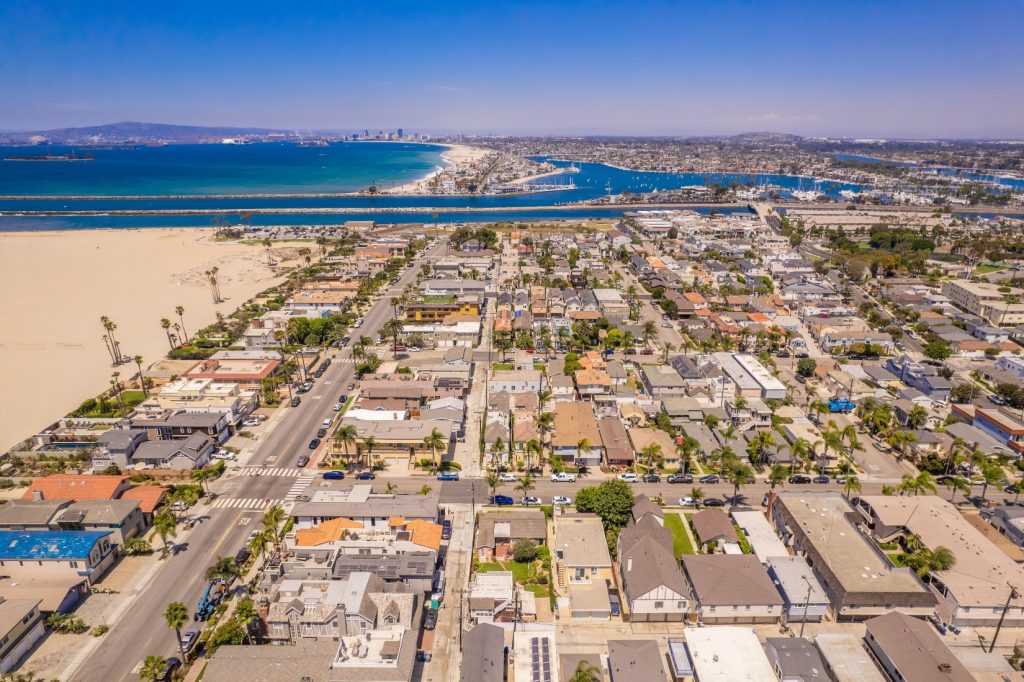 Aerial view of Seal Beach, California, featuring residential streets, sandy beaches, and a clear coastline with the Pacific Ocean under a bright blue sky.