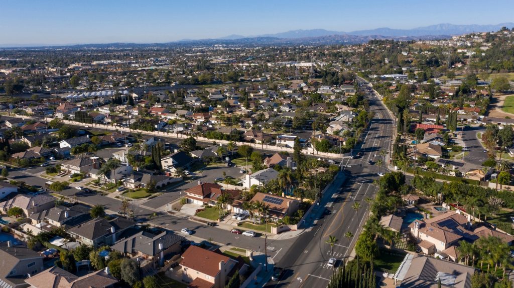 Aerial view of residential neighborhoods and tree-lined streets in Villa Park, California, with mountains visible in the distant background under a clear blue sky.
