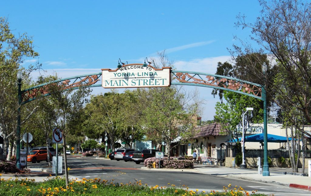 Entrance to Yorba Linda Main Street in Yorba Linda, California, featuring a decorative archway, tree-lined streets, and local shops under a sunny sky.